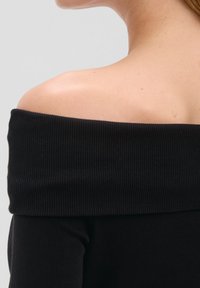 Czarny top odkrywający ramiona, wykonany z prążkowanej tkaniny, z szerokim dekoltem i dopasowanymi, długimi rękawami. Gładka tekstura i obcisły krój.