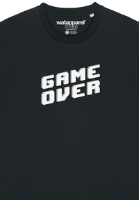 Zwarte katoenen T-shirt met een pixelachtige witte "GAME OVER" grafiek in een bloklettertype. Ronde hals met een label op de kraag.