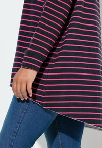 Zwart-roze gestreept langermig shirt met een gebogen zoom, gedragen over een blauwe spijkerbroek, met een zachte stoftextuur en een ontspannen pasvorm.