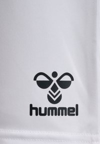 Vitt atletiskt tyg med en framträdande svart Hummel-logga, som inkluderar en stiliserad bi-design och fet text nedanför.