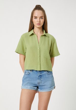Light green short-sleeve button-up shirt with a textured fabric, spread collar, and small front pocket, paired with cuffed denim shorts.