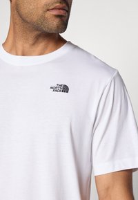 Λευκό βαμβακερό T-shirt με μικρό μαύρο κεντητό λογότυπο στο αριστερό στήθος. Στρογγυλή λαιμόκοψη και κοντά μανίκια με ομ αλή υφή.