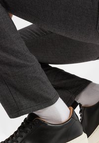 Szare spodnie w wzory o teksturowanej powierzchni, połączone z czarnymi sneakersami z jasnobrązowym akcentem na pięcie oraz białymi skarpetkami.