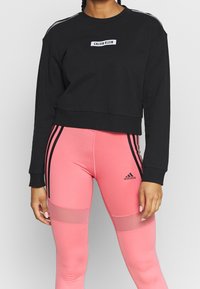 Sweatshirt noir court avec le logo "Calvin Klein", associé à des leggings roses avec des rayures noires et des panneaux en maille pour la respirabilité.