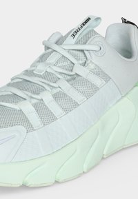 Λευκό παπούτσι Nike Free με επάνω μέρος από διχτυωτό υλικό, παχιά τμηματική σόλα και λευκά κορδόνια περασμένα μέσα από υφασμάτινους κρίκους.