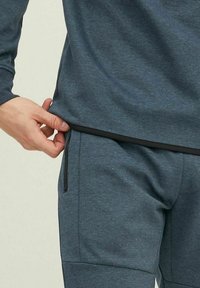 Herrarnas träningskläder med en mörkblå långärmad topp och matchande sweatpants med dragkedjefickor och kontrasterande svarta detaljer.