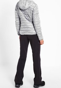 Srebrna kurtka puchowa z kapturem, pikowana, czarne spodnie outdoorowe i obuwie. Kurtka ma dopasowany krój i lekki design.