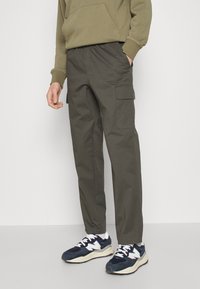 Olivegröna cargobyxor i tyg med elastisk midja, som har sidofickor och lös passform. Bärs med mörkblå sneakers.