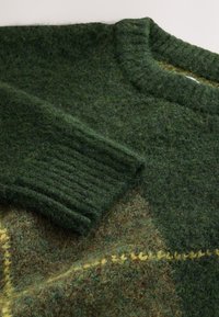 Green knitted sweater featuring ribbed cuffs, textured fabric with blended hues of green and brown, and yellow stitching detail.