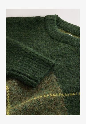 Pull vert en tricot avec poignets côtelés, tissu texturé aux teintes mélangées de vert et de marron, et détail de surpiqûres jaunes.