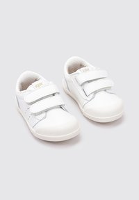 Zapatillas blancas para niños con dos correas de velcro, suela de goma texturizada y sutiles acentos grises en los lados. Logo de la marca en dorado.
