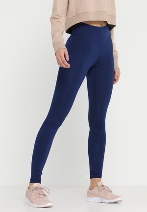 Mørkeblå leggings med høj talje, glat tekstur og tætsiddende pasform, parret med en cropped beige sweatshirt og lyserøde sneakers.