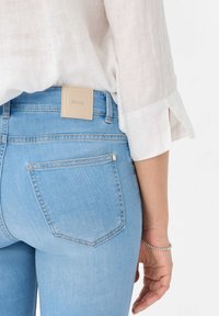 Jean en denim bleu clair à la coupe près du corps, avec un patch de marque en cuir beige carré à l'arrière et deux poches arrière.