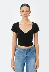 Top corto nero con maniche corte e scollo a V profondo, con un design frontale attorcigliato. Abbinato a jeans azzurri a vita alta.