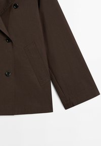 Brown, double-breasted jacket made from smooth fabric. Features large black buttons and a single side pocket. Simple, structured design.