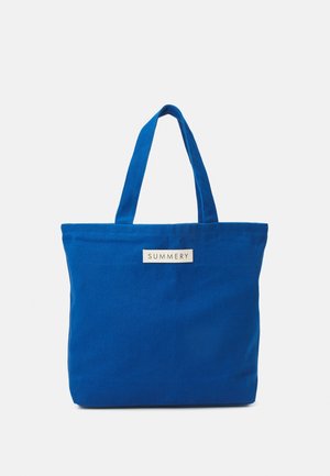Sininen kangaskassi, jossa on kaksi kahvaa ja valkoinen etiketti, jossa lukee "SUMMERY", yksinkertaisella valkoisella taustalla.