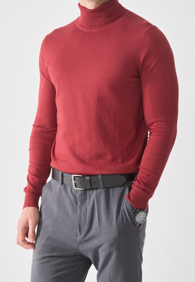 Jersey de cuello alto rojo hecho de tela suave, con mangas largas y diseño ajustado, combinado con pantalones grises y un cinturón negro.