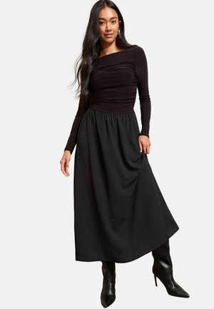 Černé dlouhé šaty s těsným korzetem a nařaseným pasem, přecházející do plné sukně. Nosené s elegantními černými špičatými botami.
