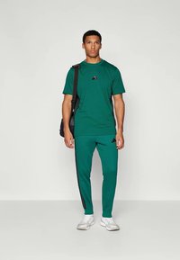Pachet sportiv pentru bărbați din material verde închis. Cămașă cu mânecă scurtă cu un mic logo negru, asortată cu pantaloni care au dungi negre pe lateral.