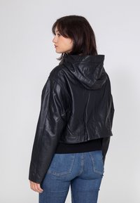 Schwarze Lederjacke mit Kapuze, aus glattem Material und lockerer Passform, kombiniert mit blauen Jeans.