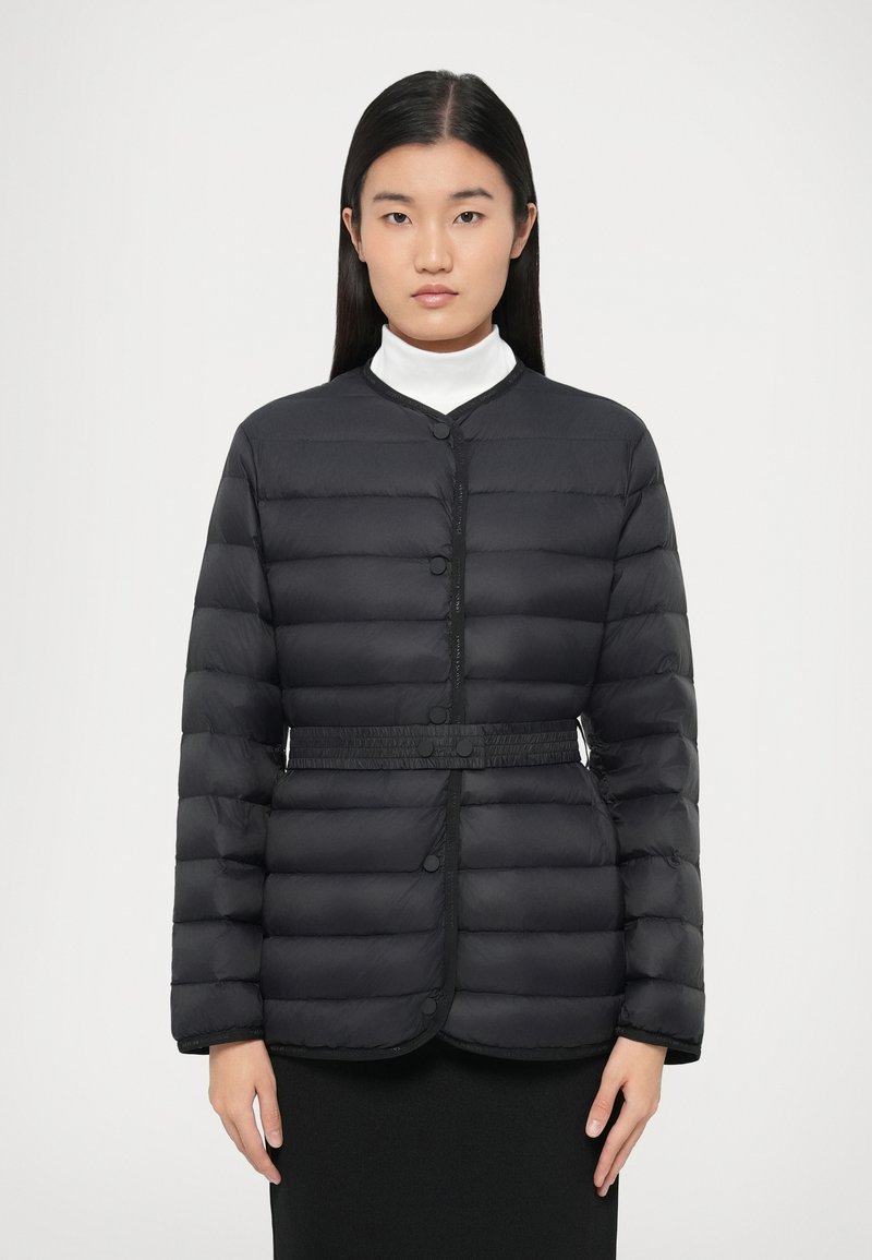 Svart polstret jakke med knappelukking, rund hals og beltedetalj. Jevn tekstur med horisontalt quiltet design.