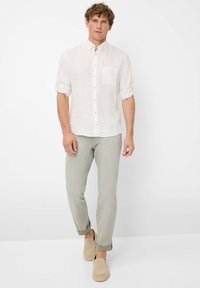 Witte linnen overhemd met korte opgerolde mouwen, borstzak, gecombineerd met lichtgroene slim-fit broek en beige instappers.