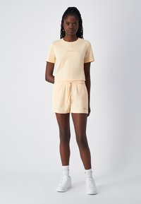 Pomarańczowa koszulka Champion i pasujące szorty wykonane z miękkiego materiału, z elastycznym pasem i akcentami logo. Białe sneakersy dopełniają stylizację.