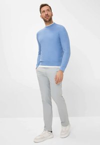 Lichtblauwe trui met een ronde hals, gecombineerd met lichtgrijze broek. Het model draagt witte sneakers, die een soepele textuur en pasvorm tonen.