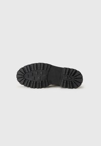 Suela de zapato de goma negra con un patrón de relieve profundo y formas triangulares elevadas. Diseño plano con superficie texturizada para un mejor agarre.