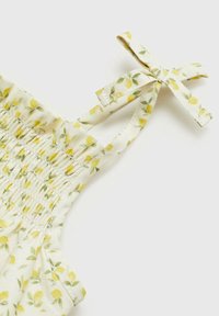 Cvetna bluza z vzorcem limon v rumeni in zeleni barvi na svetlem materialu, z nabranim gubanim in nastavljivimi naramnicami, ki so zavezane v mašne.
