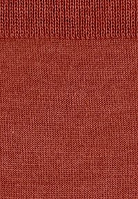Tessuto lavorato a maglia in un colore terracotta smorzato, che mostra una fine trama con un bordo superiore a costine e un corpo liscio.
