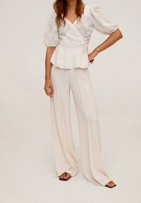 Top peplum bianco in pizzo con maniche a sbuffo abbinato a pantaloni larghi avorio, caratterizzati da una texture liscia e un design fluido.