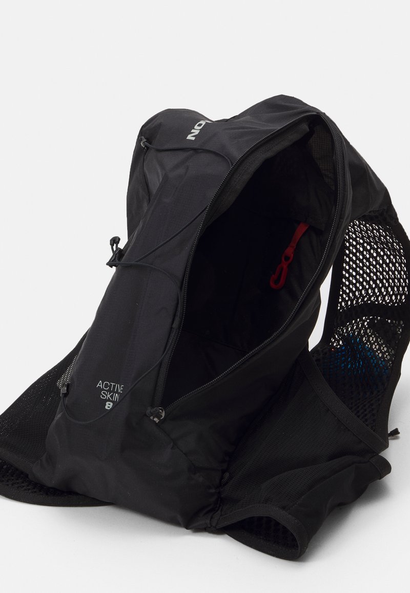 Zaino nero con schienale in rete, dotato di compartimento principale con zip, cuciture robuste e un manico rosso. Design leggero e compatto.