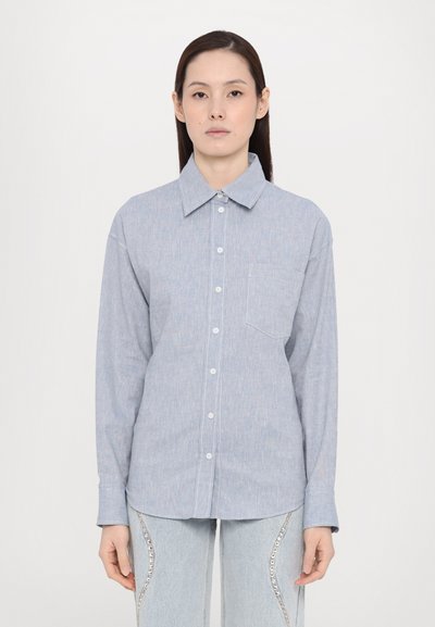 Lichtblauw overhemd met lange mouwen, knoopsluiting aan de voorkant, kraag, een enkele borstzak en een subtiele textuur. Gecombineerd met lichtblauwe jeans met versieringen.