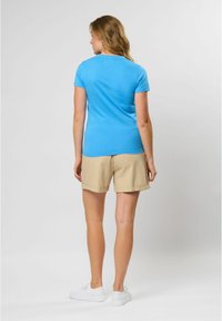 Blauwe t-shirt met korte mouwen, gecombineerd met beige shorts, met een ontspannen pasvorm en zachte textuur, tegen een lichtgrijze achtergrond.