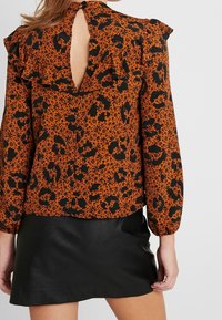 Blusa a maniche lunghe arancione con stampa floreale e animale nera, con schiena a chiave e spalle arricciate. Abbinata a una gonna in pelle nera.