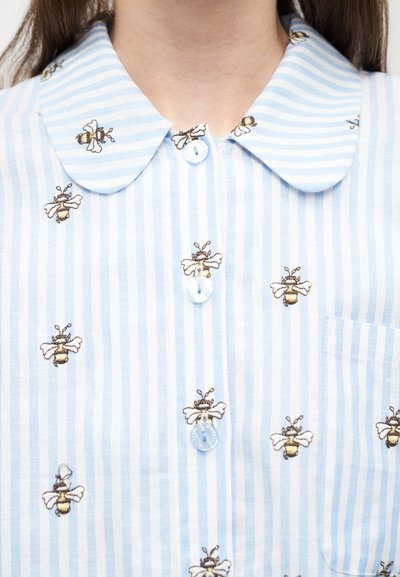 Light blue and white striped shirt with embroidered bee patterns and round collar, shown from neck to mid-chest.