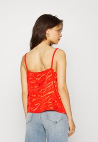 Top de seda vermelha com textura ondulada e alças finas, apresentando um corte solto que cai elegantemente. A vista traseira mostra um design simples.