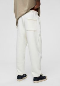 Witte joggingsbroek van zachte stof, met een enkele achterzak en een elastische tailleband. Gestyled met zwarte sneakers.