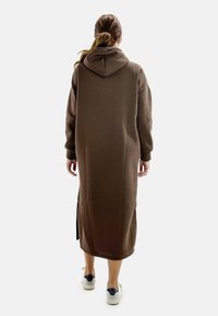 Abito cappuccio marrone con maniche lunghe, spacco laterale e vestibilità ampia. Realizzato in tessuto morbido, arriva a metà polpaccio.