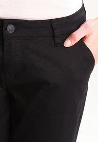 Black cotton-blend pants with a smooth texture, front pocket detail, and a metal button closure at the waist.