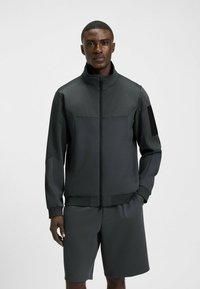 Idrottsjacka och short-set i mörkgrått, med hög krage, dragkedjestängning, texturerade accenter och elastisk midja.