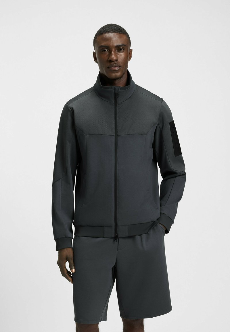 Idrottsjacka och short-set i mörkgrått, med hög krage, dragkedjestängning, texturerade accenter och elastisk midja.