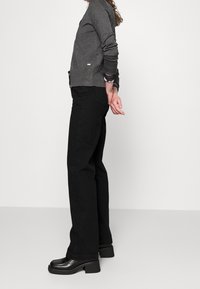 Szary kardigan z okrągłym kołnierzem, zestawiony z czarnymi spodniami z wysokim stanem. Całość uzupełniają czarne buty na masywnym obcasie.