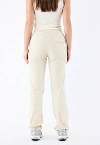 Pantaloni jogger beige con una vestibilità comoda, vita elastica e una tasca sul retro. Il materiale sembra morbido, con una texture liscia e leggermente lucida.