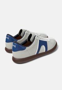 Zapatillas blancas de cuero con detalles azules y suelas de goma marrón. Presentan una forma redondeada, diseño con cordones y cuello acolchado.