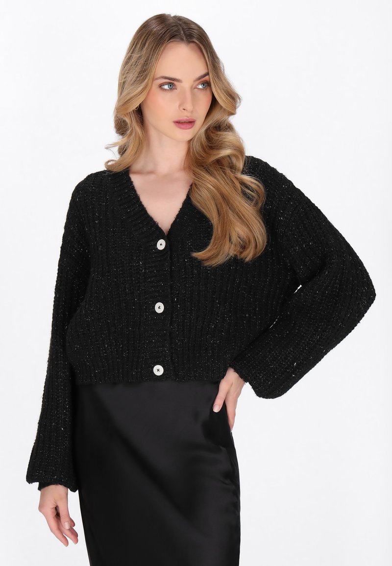 Cardigan nero corto realizzato in tessuto a maglia testurizzata, con scollatura a V, maniche lunghe e tre grandi bottoni bianchi sul davanti.