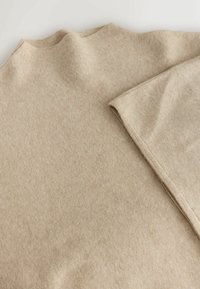 Tejido de punto beige, textura suave, con un borde doblado. Material suave y grueso diseñado para el calor, con sutiles variaciones de color.