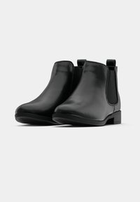 O pereche de cizme negre din piele până la gleznă, cu toc mic și panouri laterale elastice, pe un fundal alb.