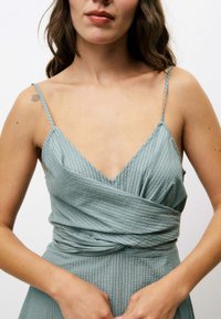Robe portefeuille vert clair avec des fines bretelles, dotée de rayures verticales et d'un décolleté en V profond, fabriquée à partir d'un tissu doux et texturé.